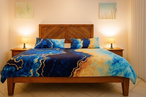 Una cama con una colcha de diseño azul y dorado, cabecera de madera, dos lámparas de noche y una mesita de noche.