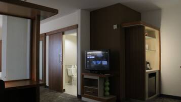 Habitación de hotel con una televisión sobre un mueble de madera, un armario pequeño y una puerta que da a un baño.