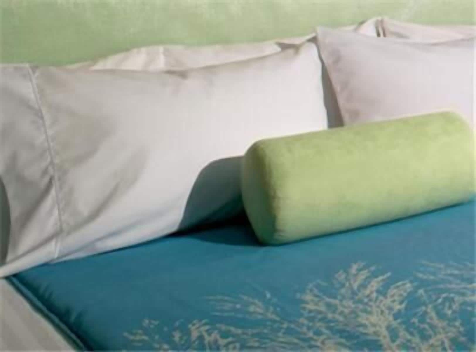 A bed with white and green pillows and a blue bedspread with a leaf pattern.