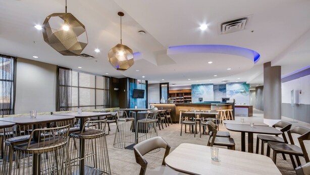 Un restaurant moderne avec des tables et des chaises rondes, un coin bar et une grande fenêtre laissant entrer la lumière naturelle.