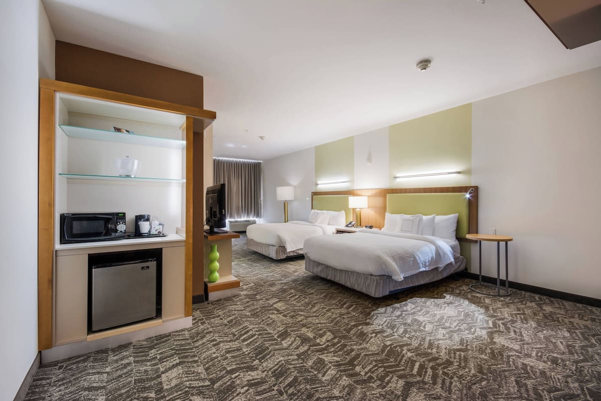 A hotel room with two beds, a microwave, a mini fridge, a TV, and a small table.