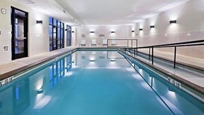 Une grande piscine intérieure à l’eau d’un bleu limpide, entourée de murs blancs et bordée d’une longue plage rectiligne.