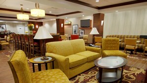 Un hall de hotel con un sofá amarillo, sillones a juego, una mesita de centro y un televisor montado en la pared.