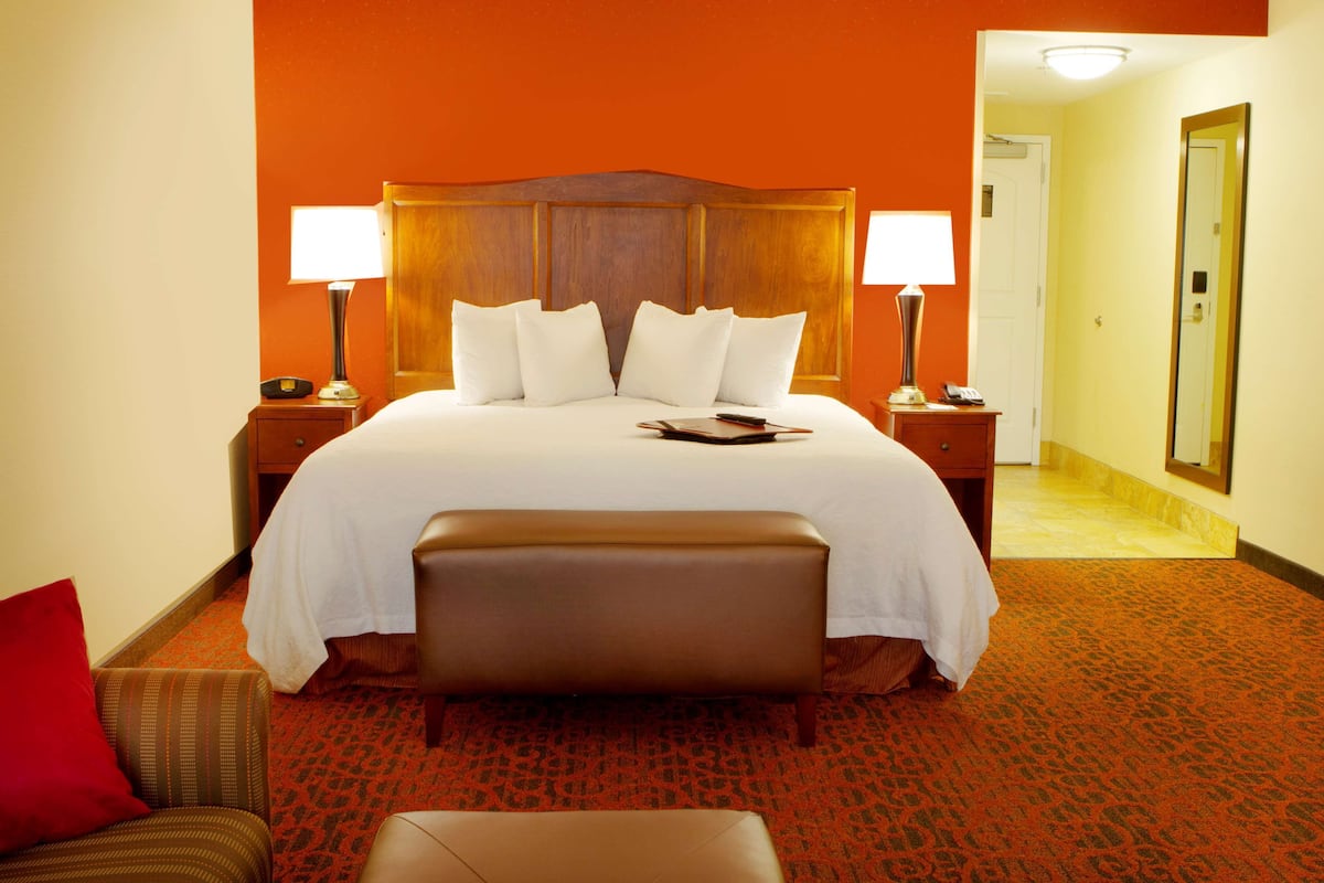 A hotel room with a large bed, two bedside tables, a nightstand, a bench, and a mirror.