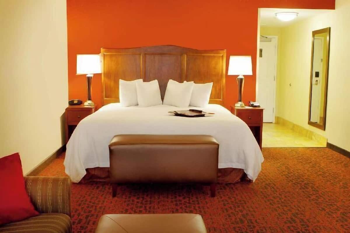 A hotel room with a large bed, two bedside tables, a bench, a red carpet, and a mirror on the wall.