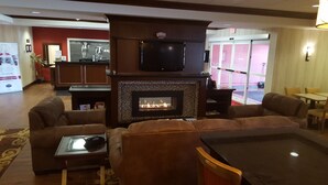 Una sala de estar con chimenea, sofás de cuero, un televisor de pantalla plana y una zona de comedor con sillas amarillas.