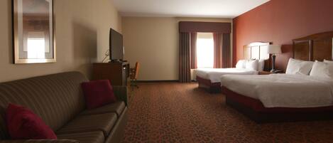 A hotel room with a sofa, two beds, a TV, and a large window with curtains.