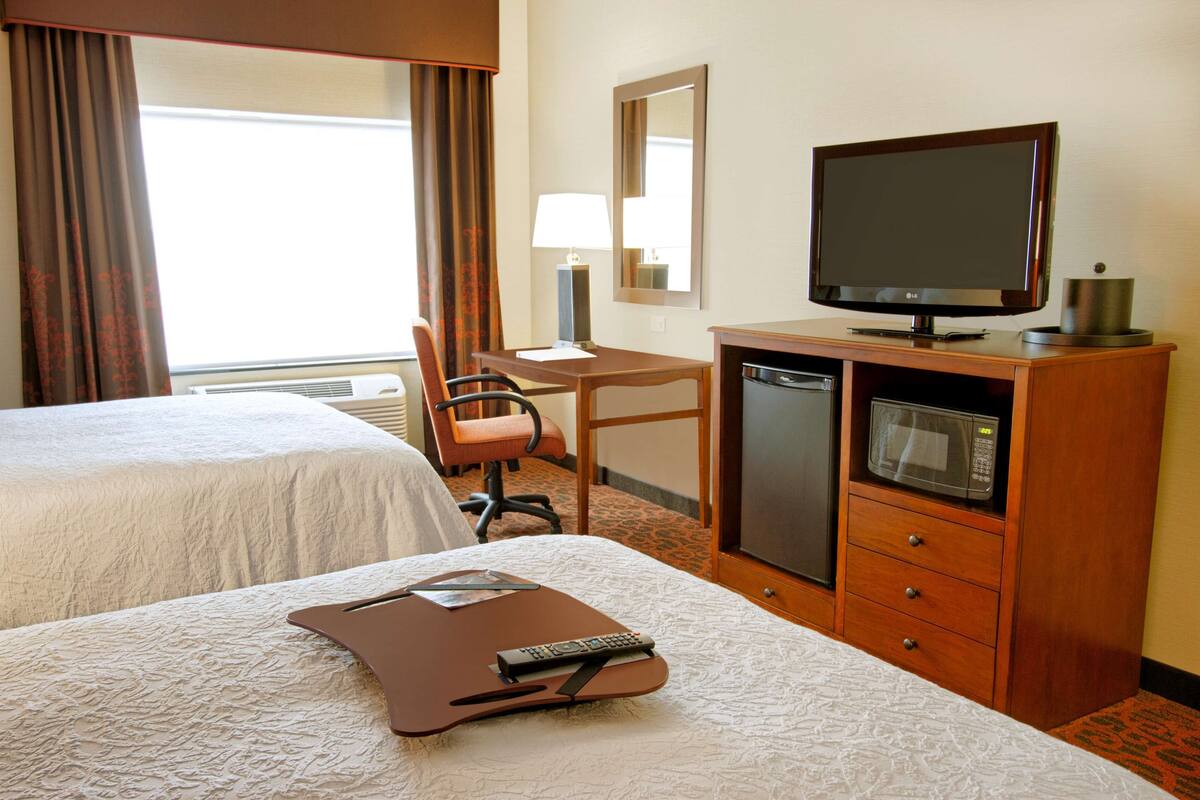 A hotel room with two beds, a desk, a chair, a television, a microwave, and a remote control.