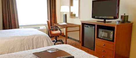 A hotel room with two beds, a desk, a chair, a television, a microwave, and a remote control.