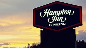A sign for Hampton Inn by Hilton with a sunset background.