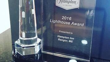 A clear award plaque with the text "2016 Lighthouse Award Presented to Hampton Inn Bangor, ME".