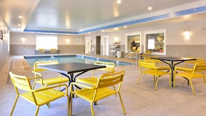 Zona de piscina con sillas y mesas amarillas, una piscina y un mostrador de recepción.