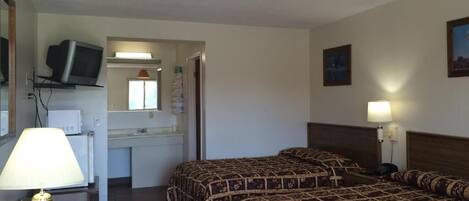 Ett hotellrum med två sängar, en tv på en hylla, ett skrivbord med en lampa och ett badrum som syns genom en öppen dörr.