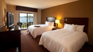 A hotel room with two beds, a TV, a desk, and a view of the water. - Hampton Inn Marquette/Waterfront (Marquette)