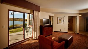 A hotel room with a large sliding glass door leading to a balcony, a television on a wooden cabinet, a red sofa, and a patterned carpet. - Hampton Inn Marquette/Waterfront (Marquette)