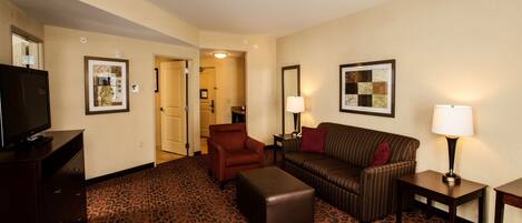 A hotel room with a sofa, armchair, ottoman, television, and two lamps.