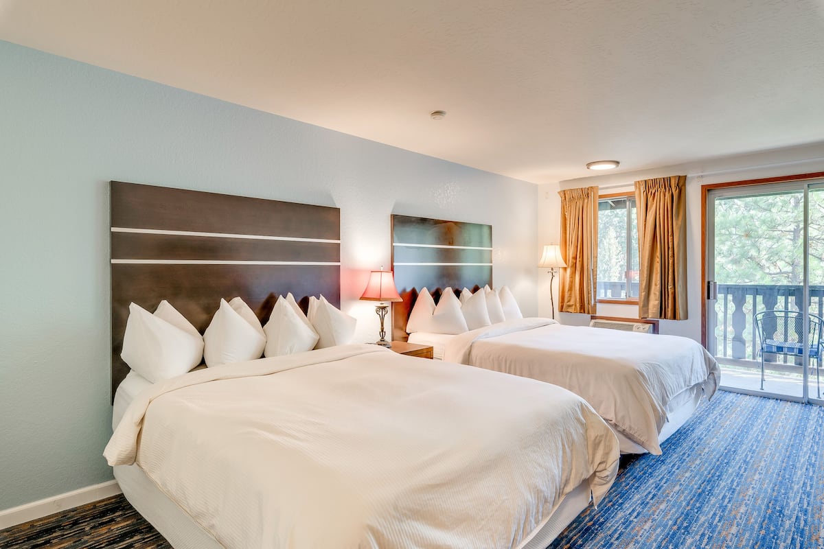 A hotel room with two beds, a large abstract painting on the wall, a window with curtains, and a view of the outdoors.