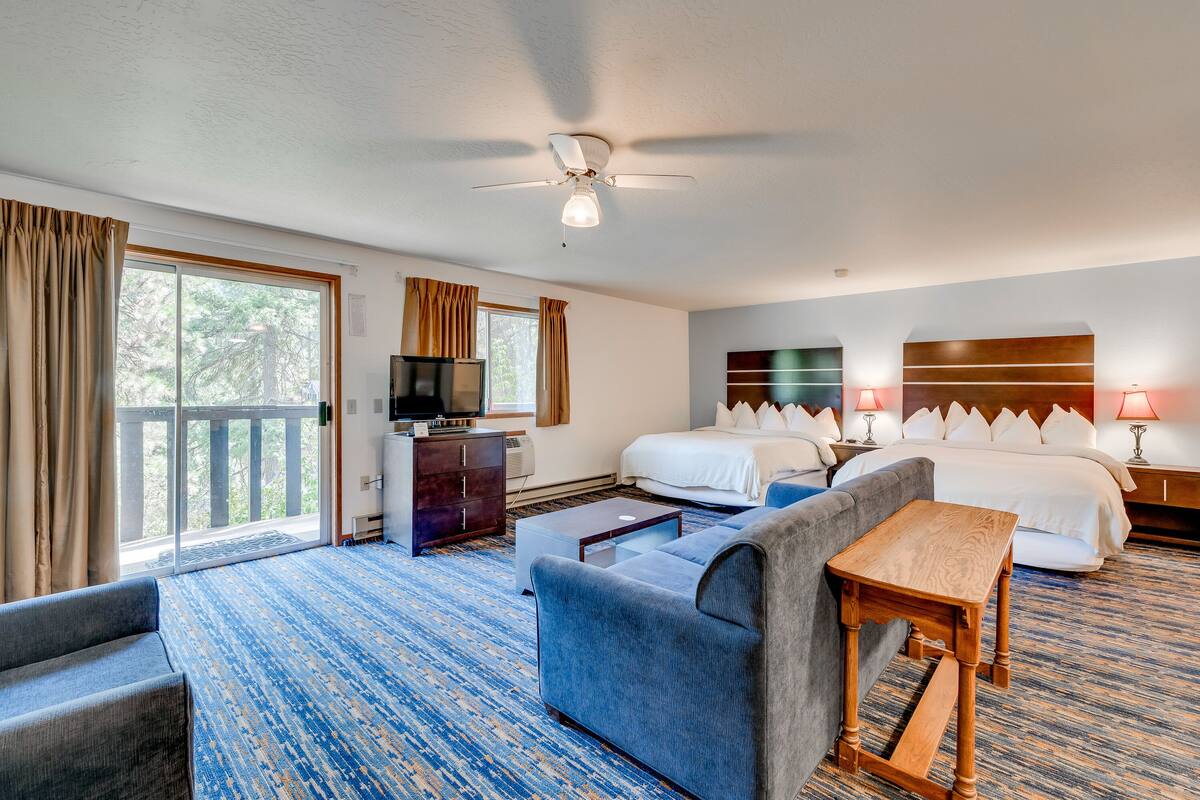 A hotel room with a large bed, a sofa, a desk, a television, and a balcony with curtains.