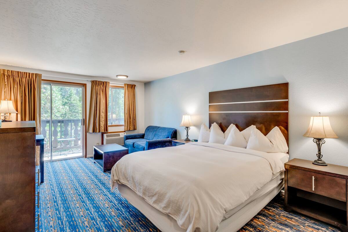 A hotel room with a large bed, a desk, a chair, and a view of the outdoors through the window.