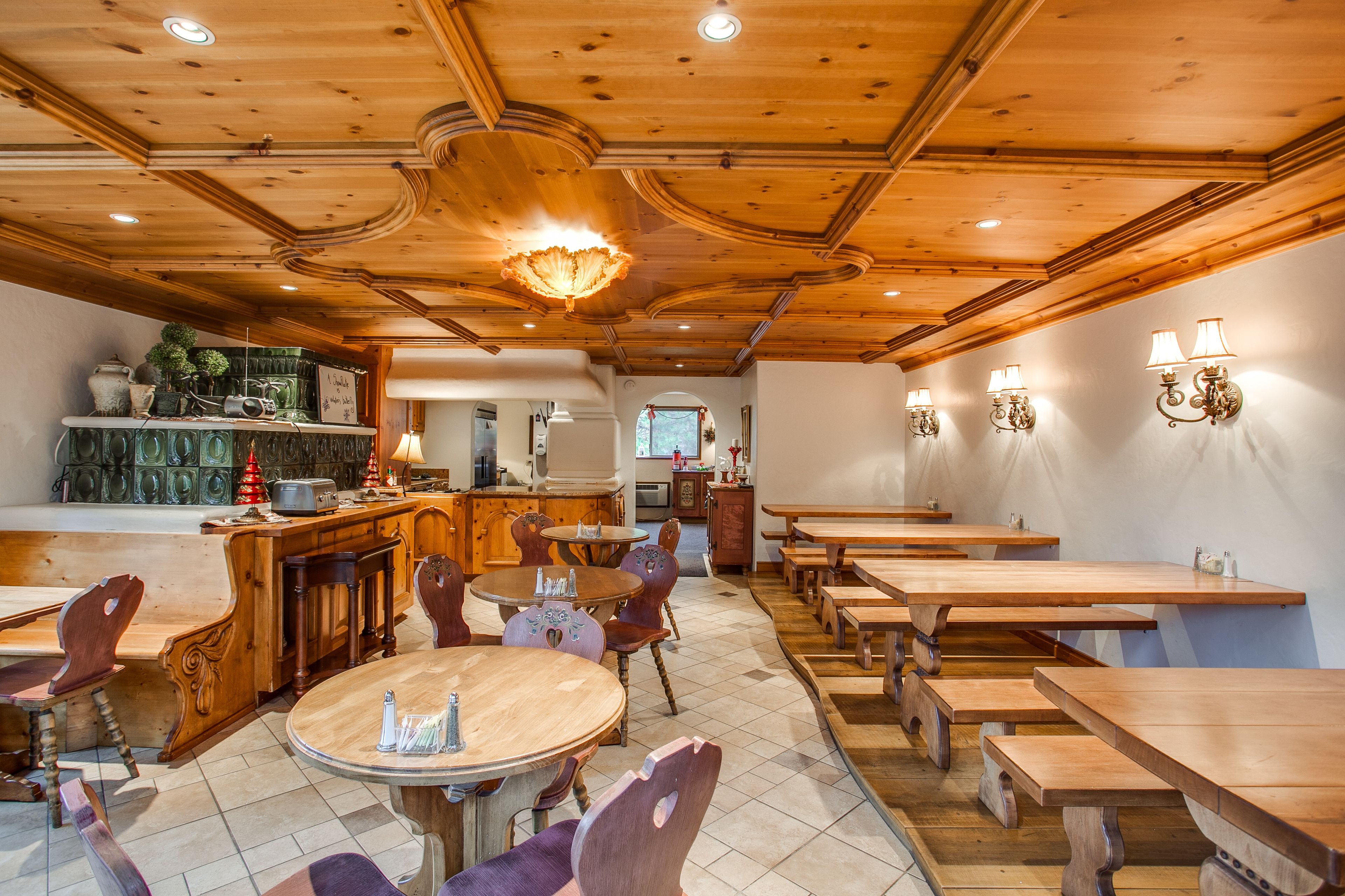 A restaurant with wooden tables and chairs, a bar area, and a kitchen visible in the background.