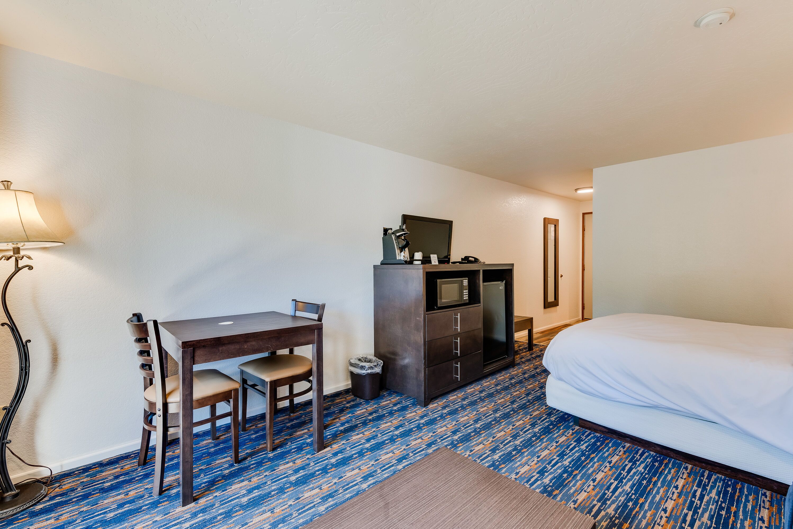 Una habitación de hotel con cama, escritorio con silla, microondas y lámpara.