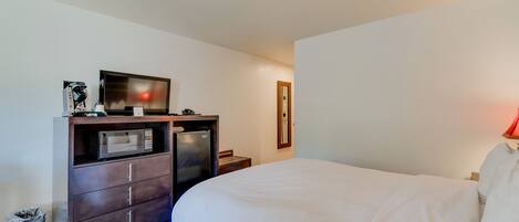 A hotel room with a bed, a desk with a microwave, a trash bin, and a mirror on the wall.