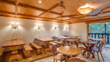 A restaurant with wooden tables and benches, wall sconces, and a large window with a view of trees.