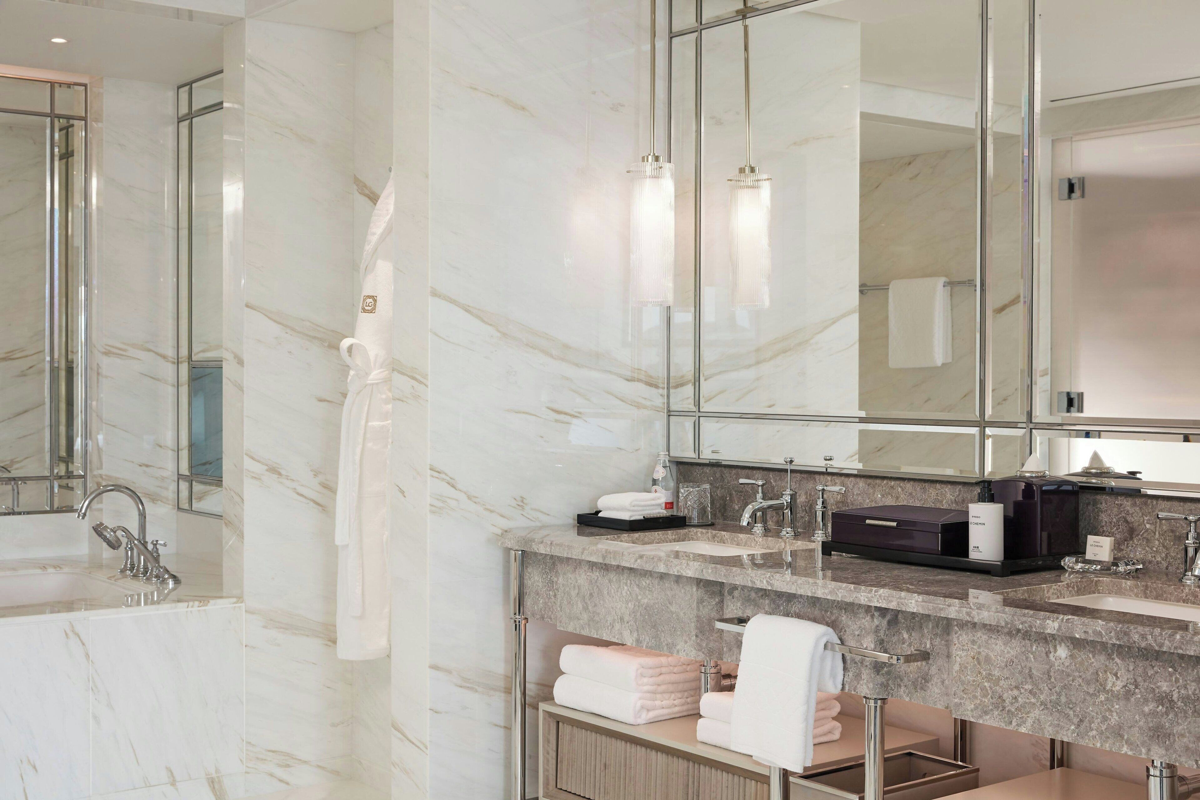 Un baño moderno con pared de mármol, un espejo grande, una bañera y un tocador con perchero.