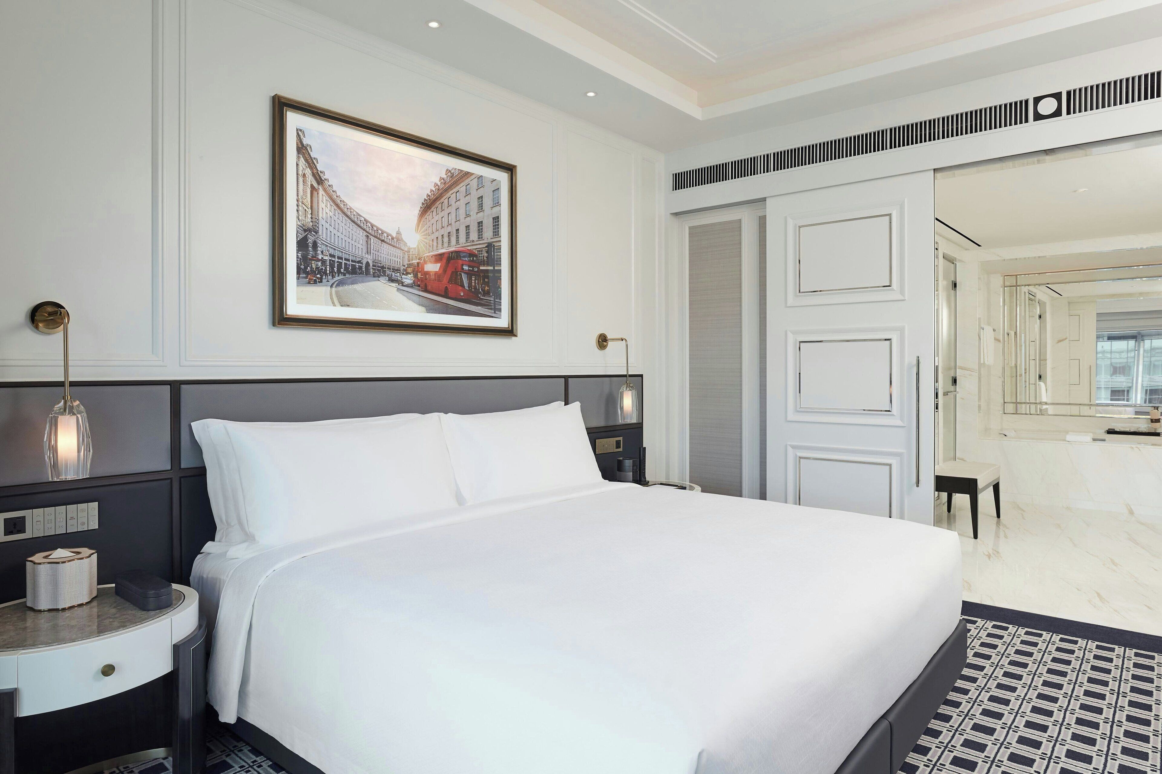Una habitación de hotel moderna con una cama grande, una mesita de noche y una imagen enmarcada en la pared, con vistas al baño.