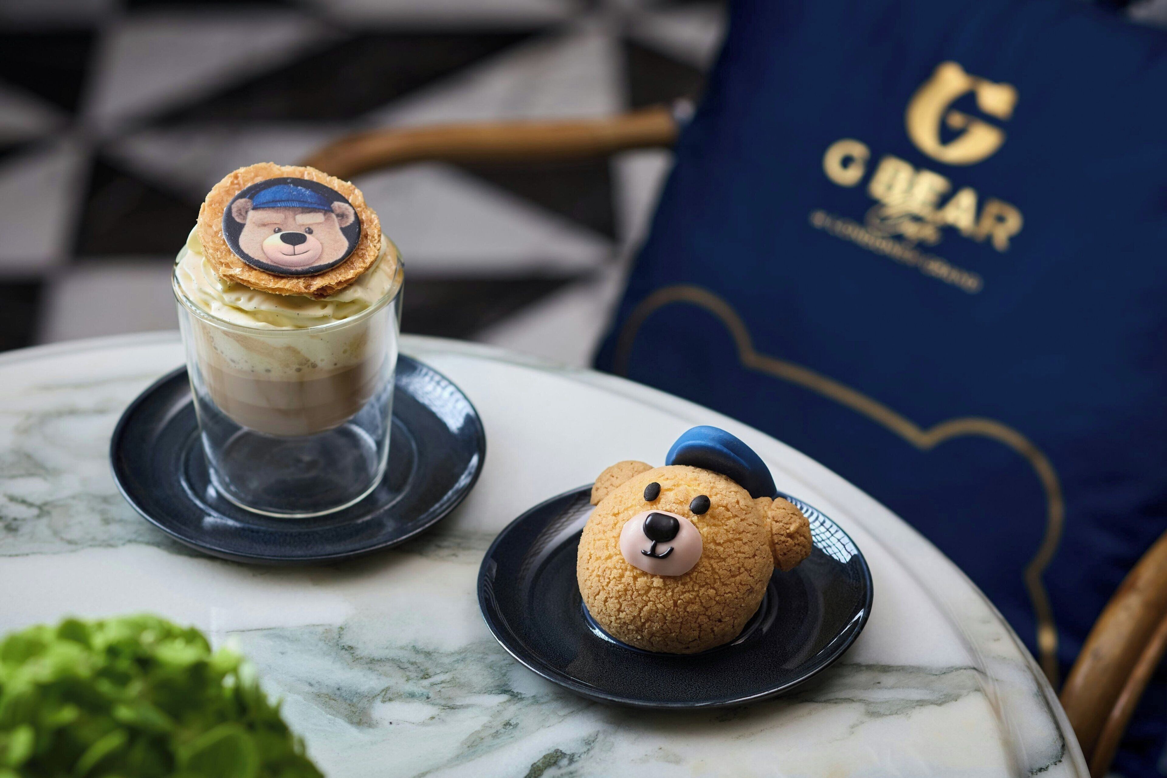 A dessert with a bear design on a plate, a glass dessert, and a bear-shaped cookie on a table.