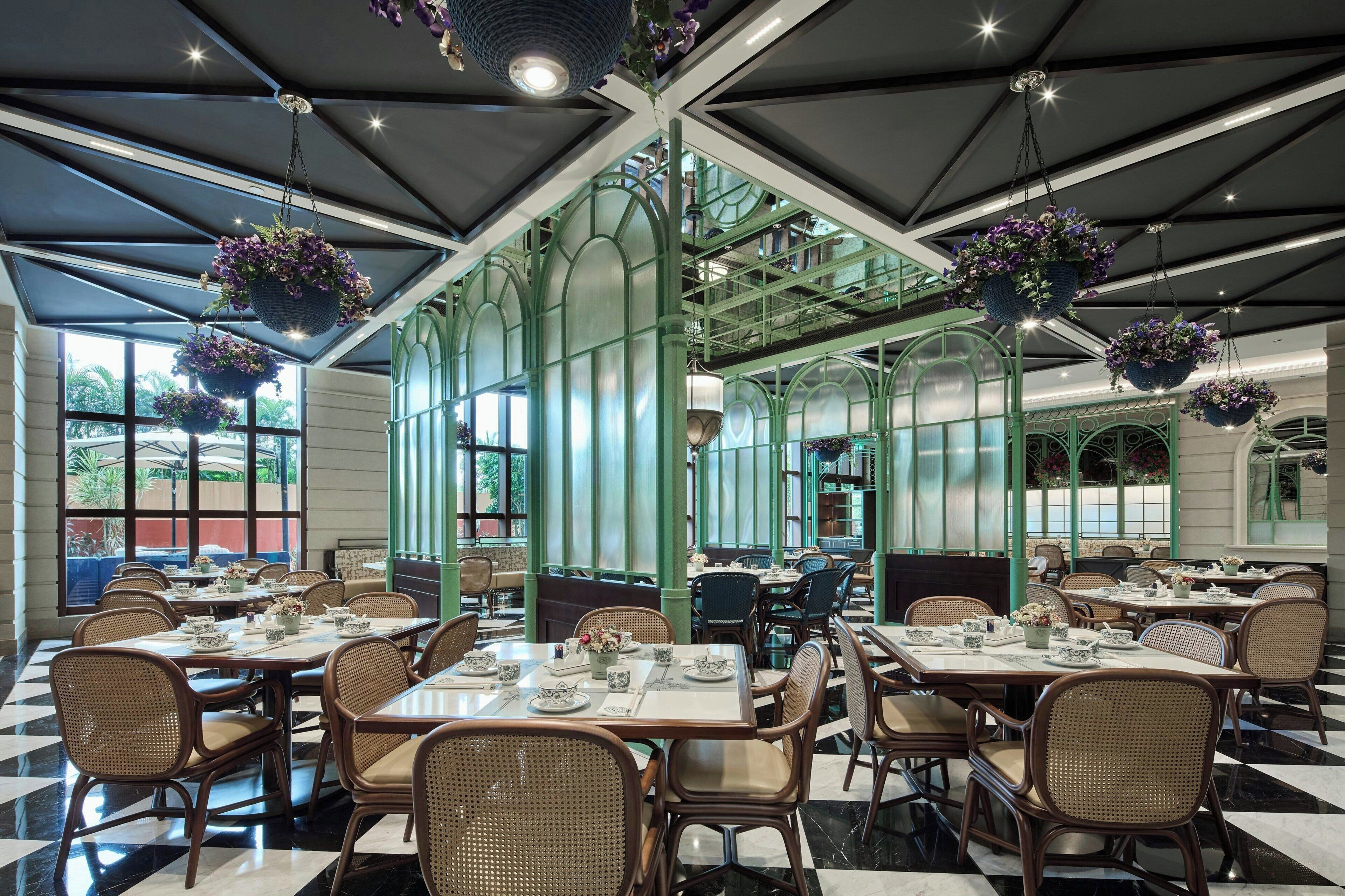 Restaurant amb sostres alts, cistells de flors penjants i un terra de taules de viqueta. Les taules estan preparades amb plats, tasses i coberts.