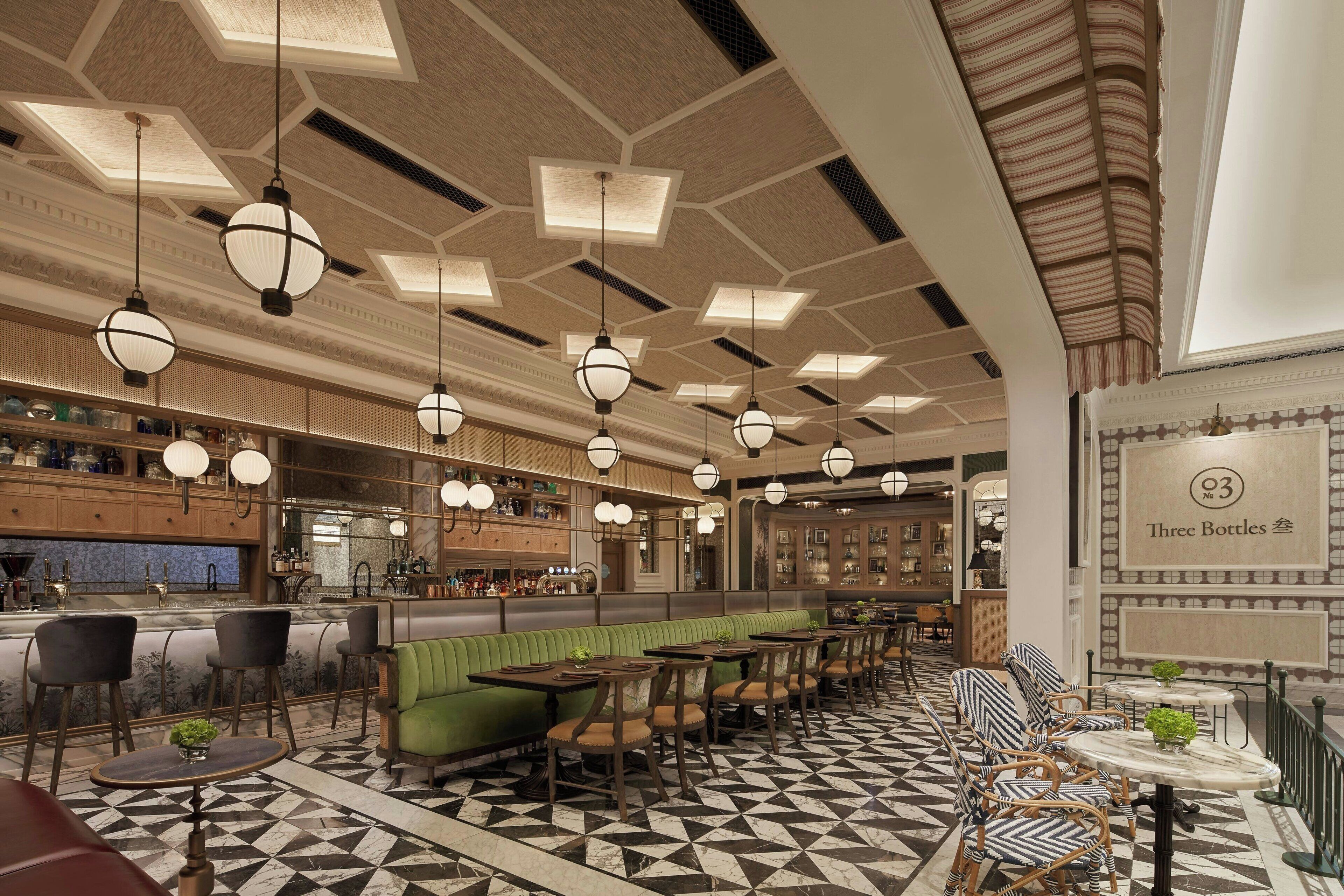 Ein Restaurant mit geometrischem Bodenmuster, grünen gepolsterten Sitzbänken und hängenden, kugelförmigen Leuchten.