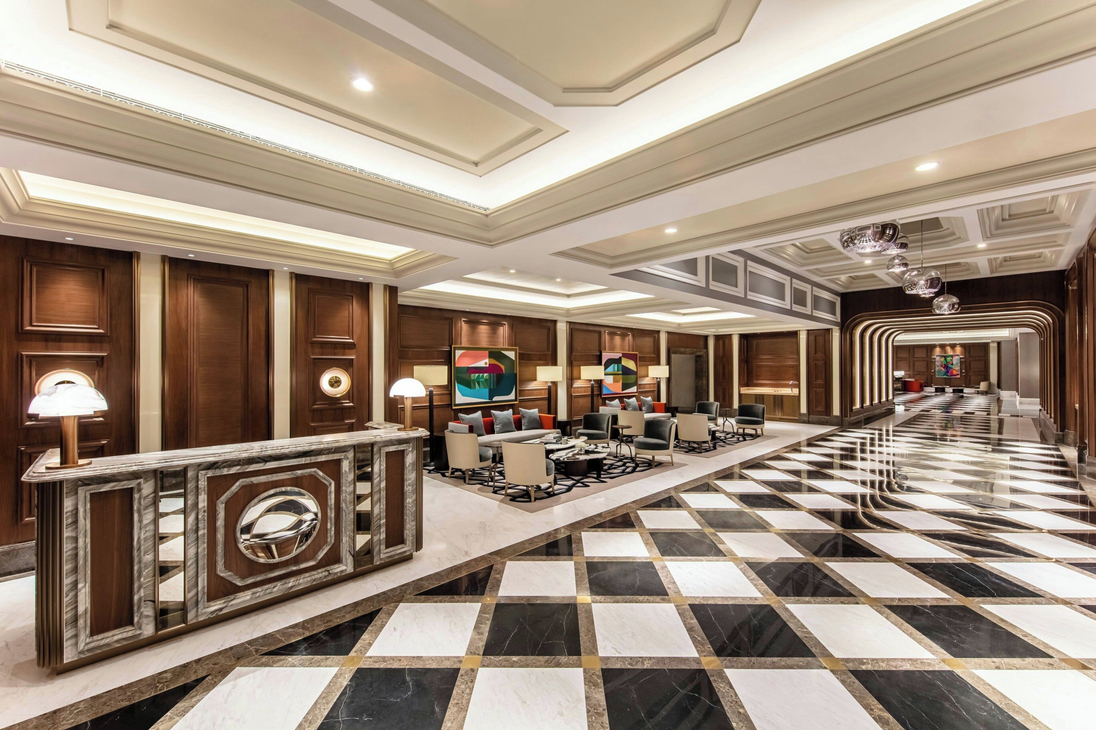 Un vestíbulo de hotel con un mostrador de recepción de mármol, zona de estar y mostradores de recepción.