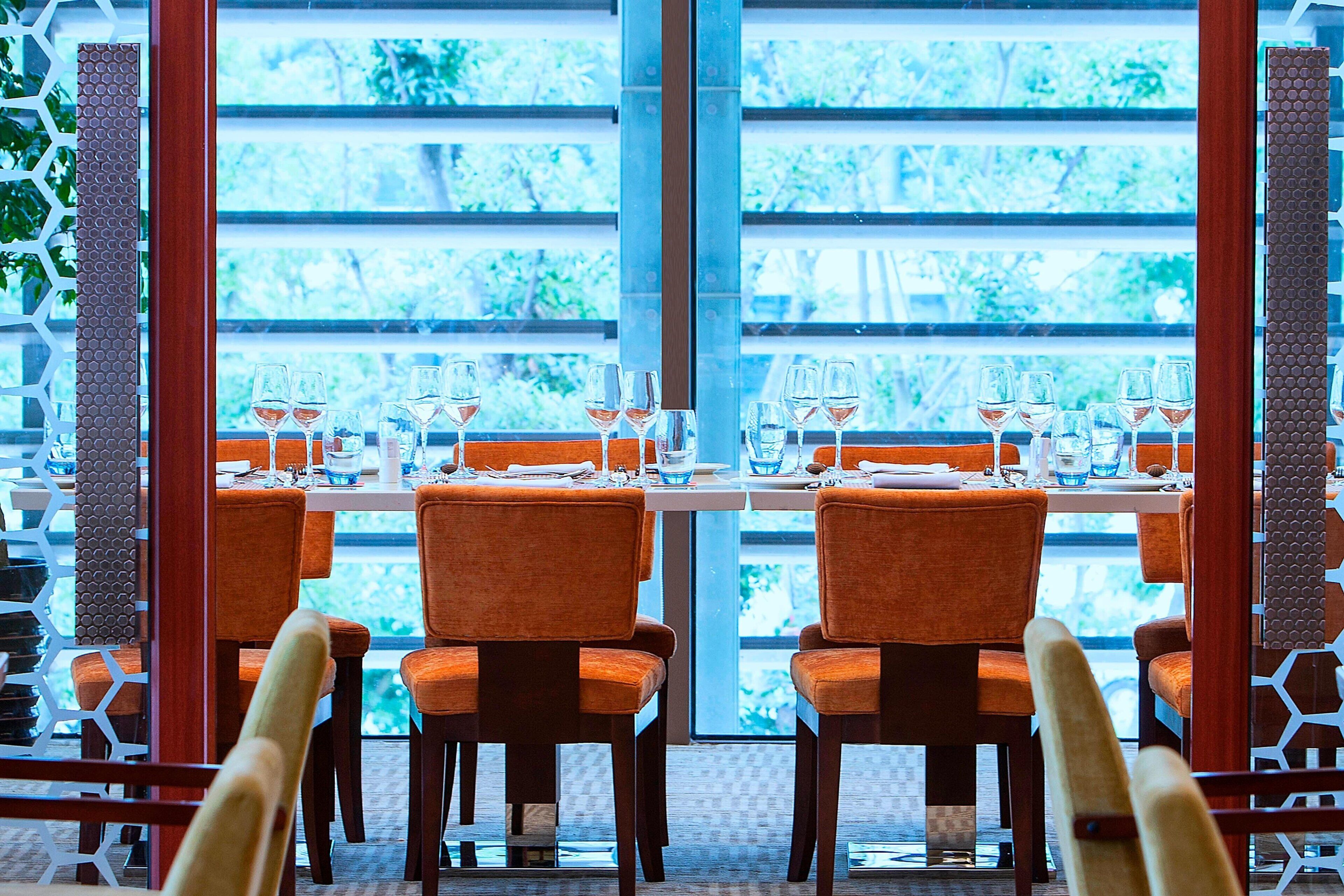Un restaurante con vistas amplias a través de grandes ventanales, mesas dispuestas con sillas y una decoración de diseño moderno.
