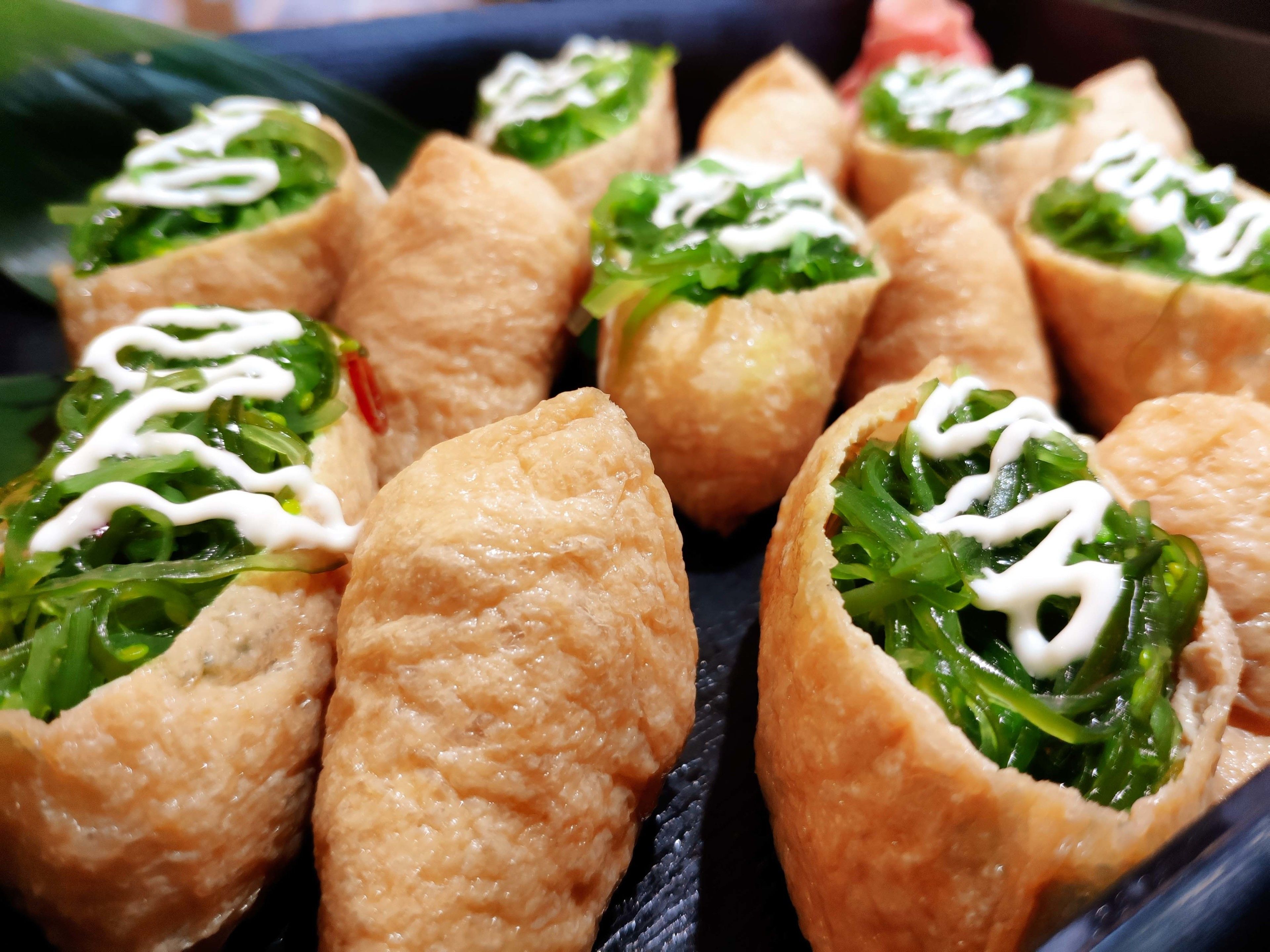 A tray of food items, likely appetizers, with a crispy outer layer and a green filling topped with a white sauce.