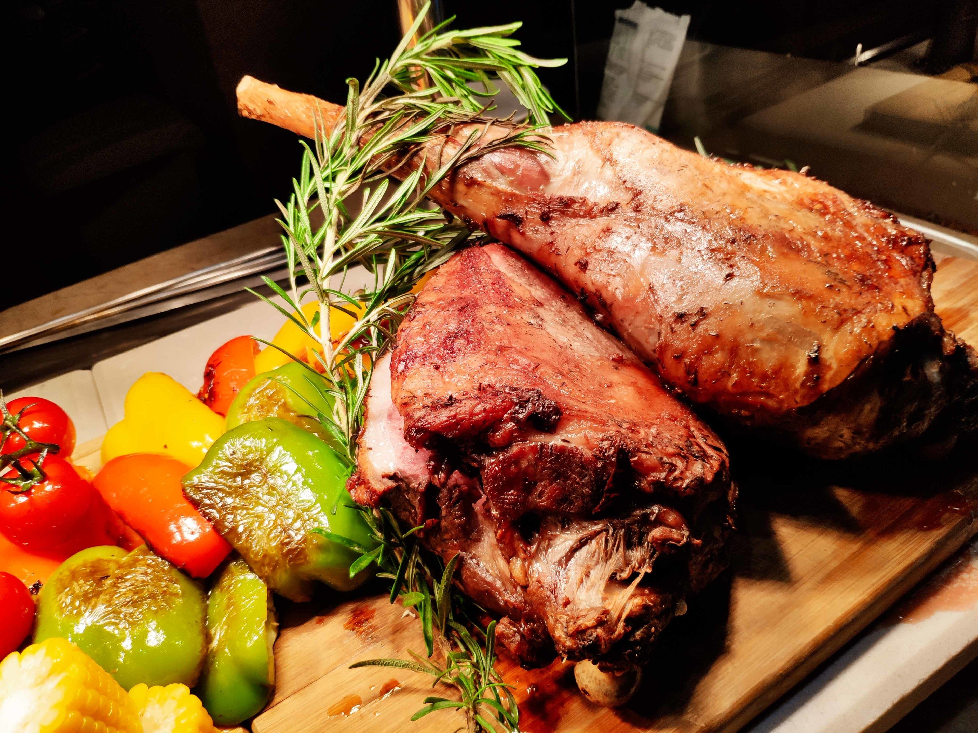 A roasted lamb leg with rosemary, accompanied by roasted vegetables on a wooden board.