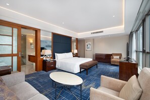 Relax in a spacious room with a large bed, sofa, and separate seating area, offering a flat-screen TV and a view of the outside.