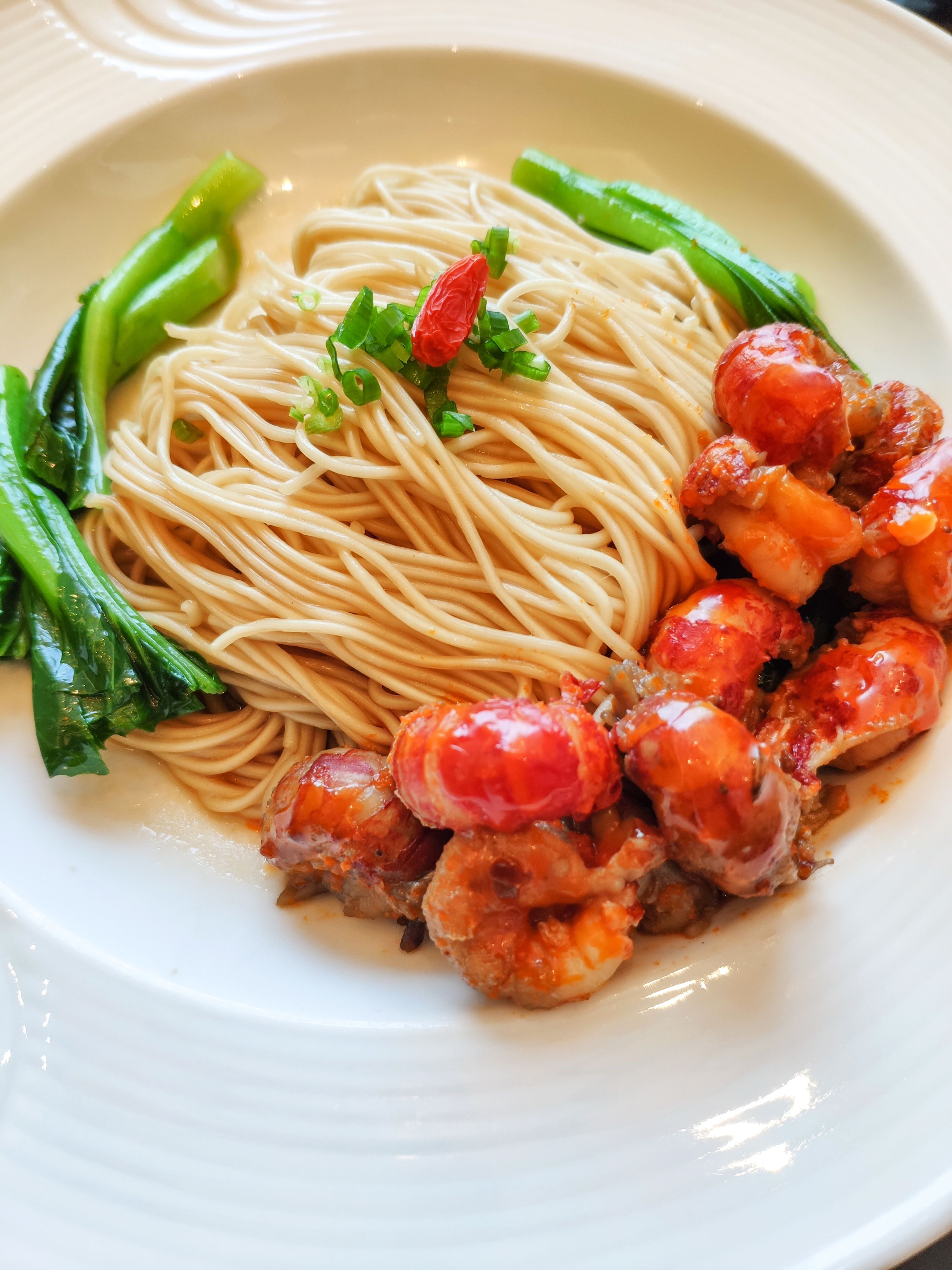 Une assiette de nouilles, de légumes verts et de crevettes.