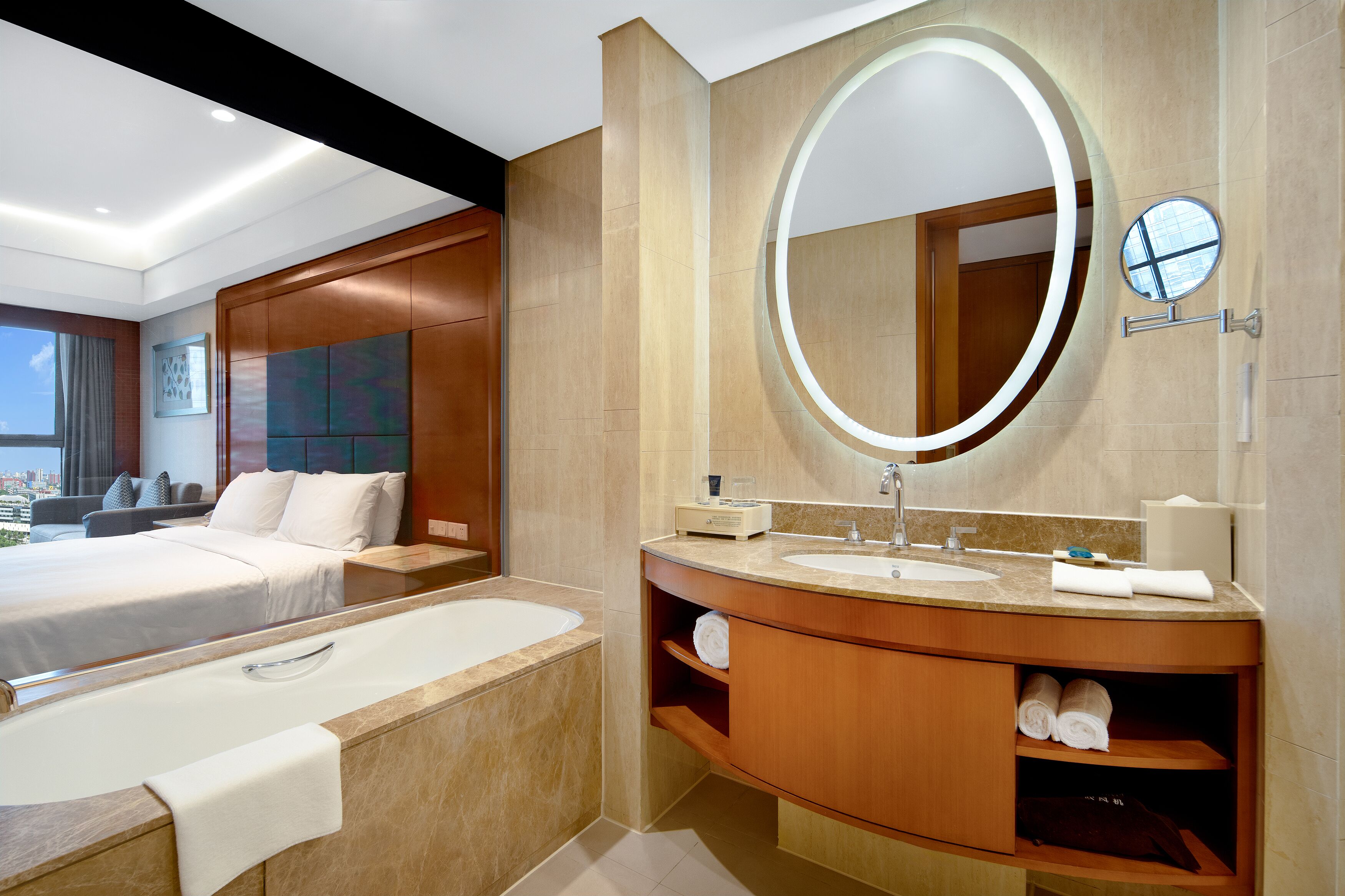 A modern hotel room with a large bed, a bathroom with a large mirror, a bathtub, and a view of the city.