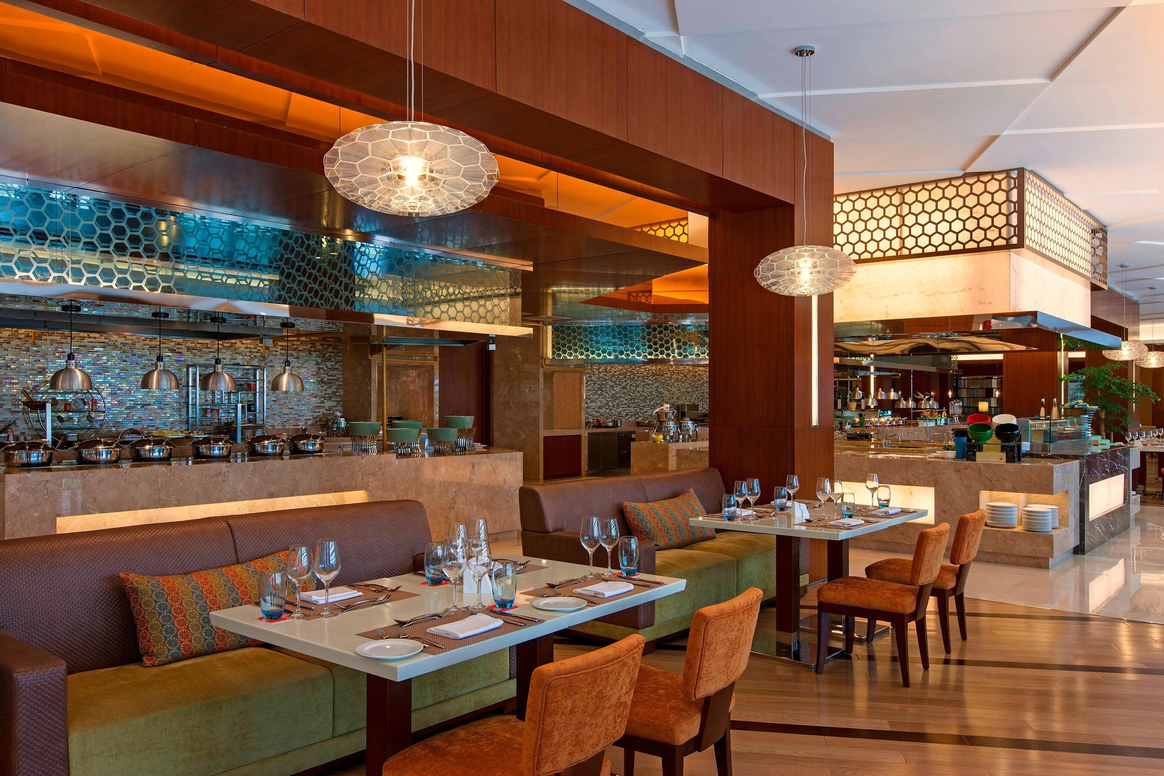 A modern restaurant with a bar area, seating arrangements, and a kitchen in the background.