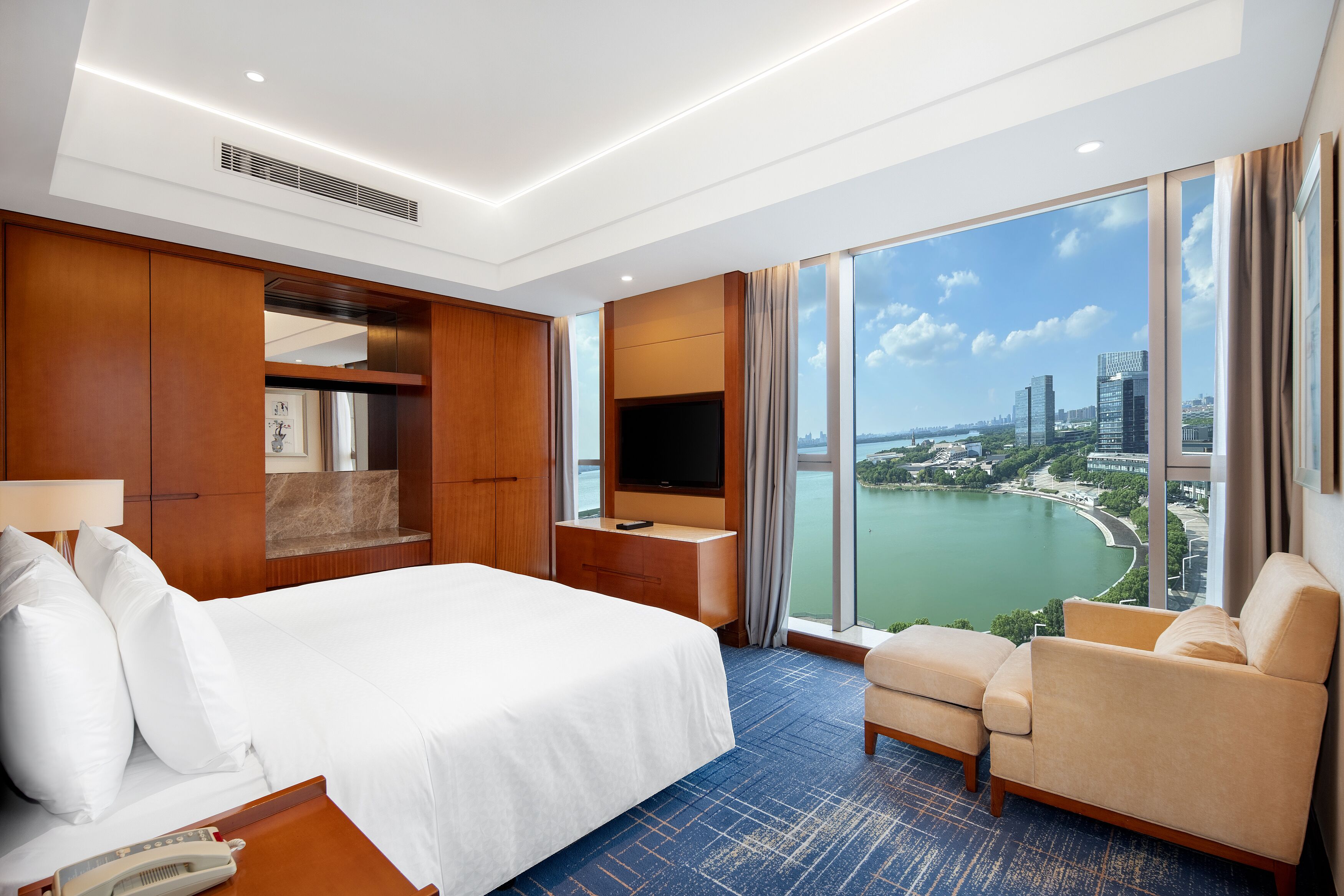 Habitación de hotel con una cama grande, televisión, escritorio y vistas a la ciudad y un lago.