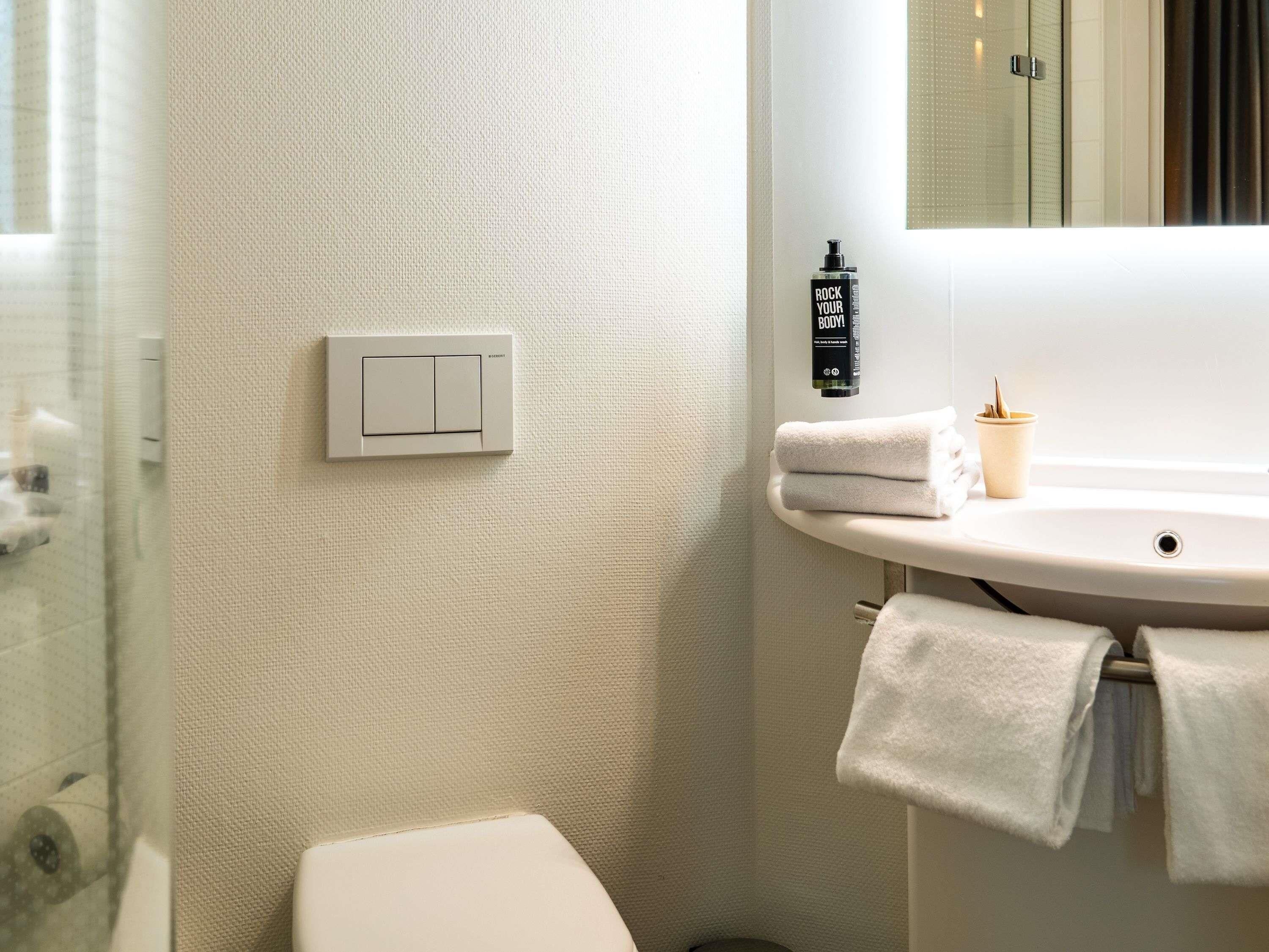 A bathroom with a white toilet, a sink with a mirror, a towel rack, and a soap dispenser.