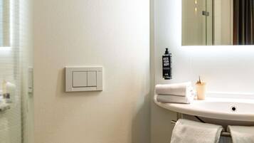 A bathroom with a white toilet, a sink with a mirror, a towel rack, and a soap dispenser.