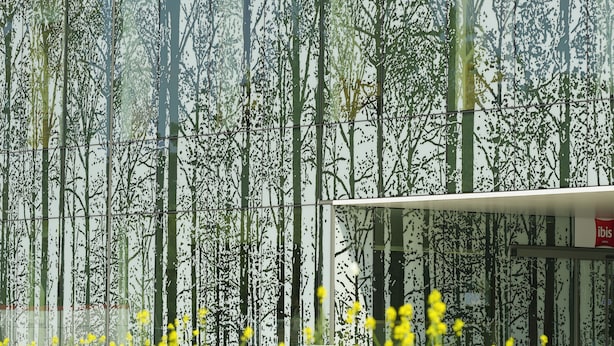 A modern building facade with vertical glass panels reflecting trees. - ibis Leuven Heverlee (Leuven)