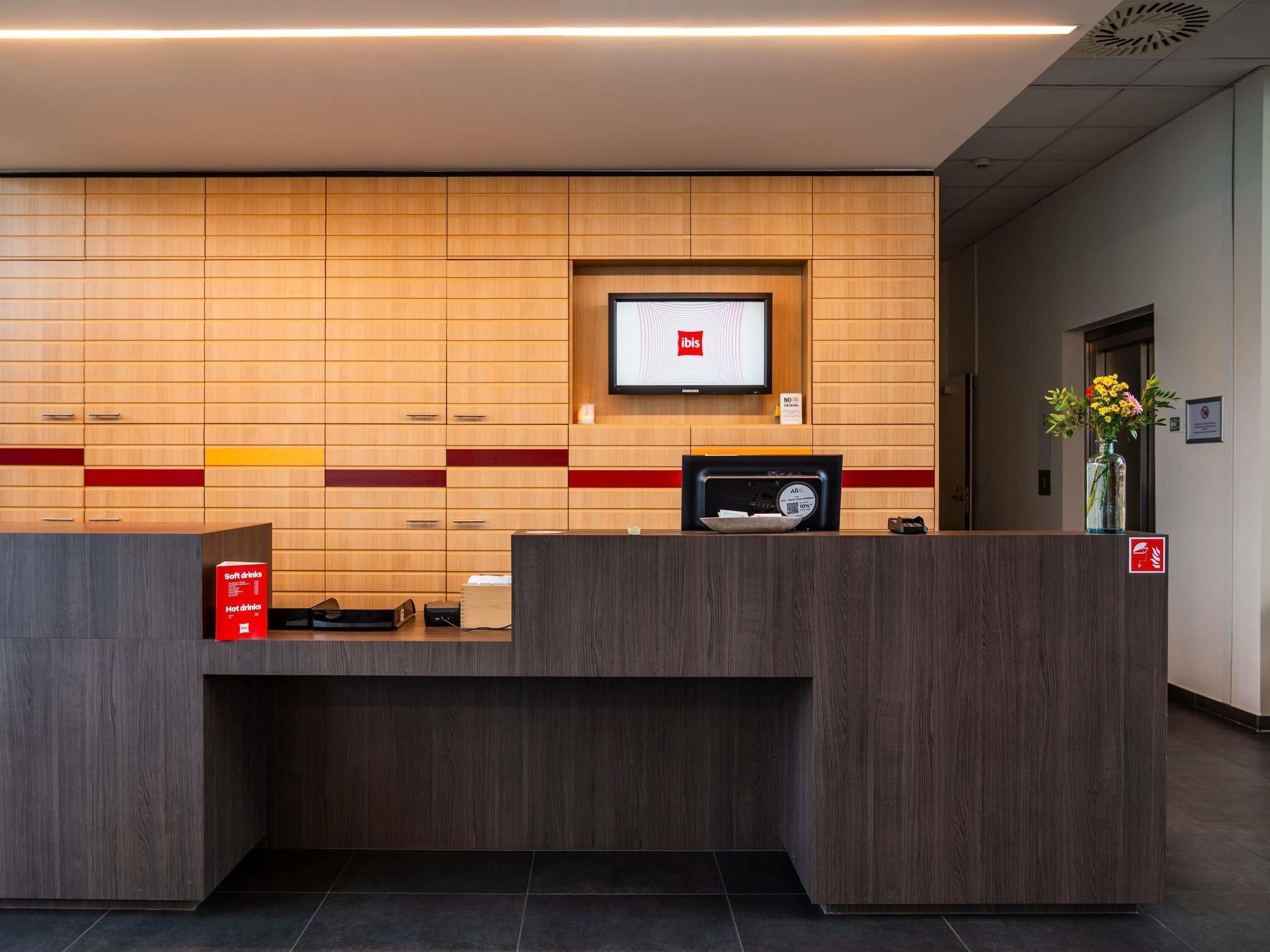 A hotel reception desk with a mounted television, a digital scale, and a sign indicating no smoking.