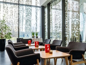 Ein modernes Interieur mit Sitzgelegenheiten, Tischen und großen Fenstern mit dekorativen Mustern.