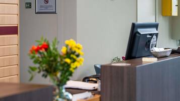 A reception desk with a framed sign, a computer monitor, and a vase with flowers.