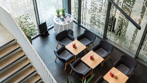 A modern indoor space with a staircase, a seating area with tables and chairs, and a view through large windows. - ibis Leuven Heverlee (Leuven)