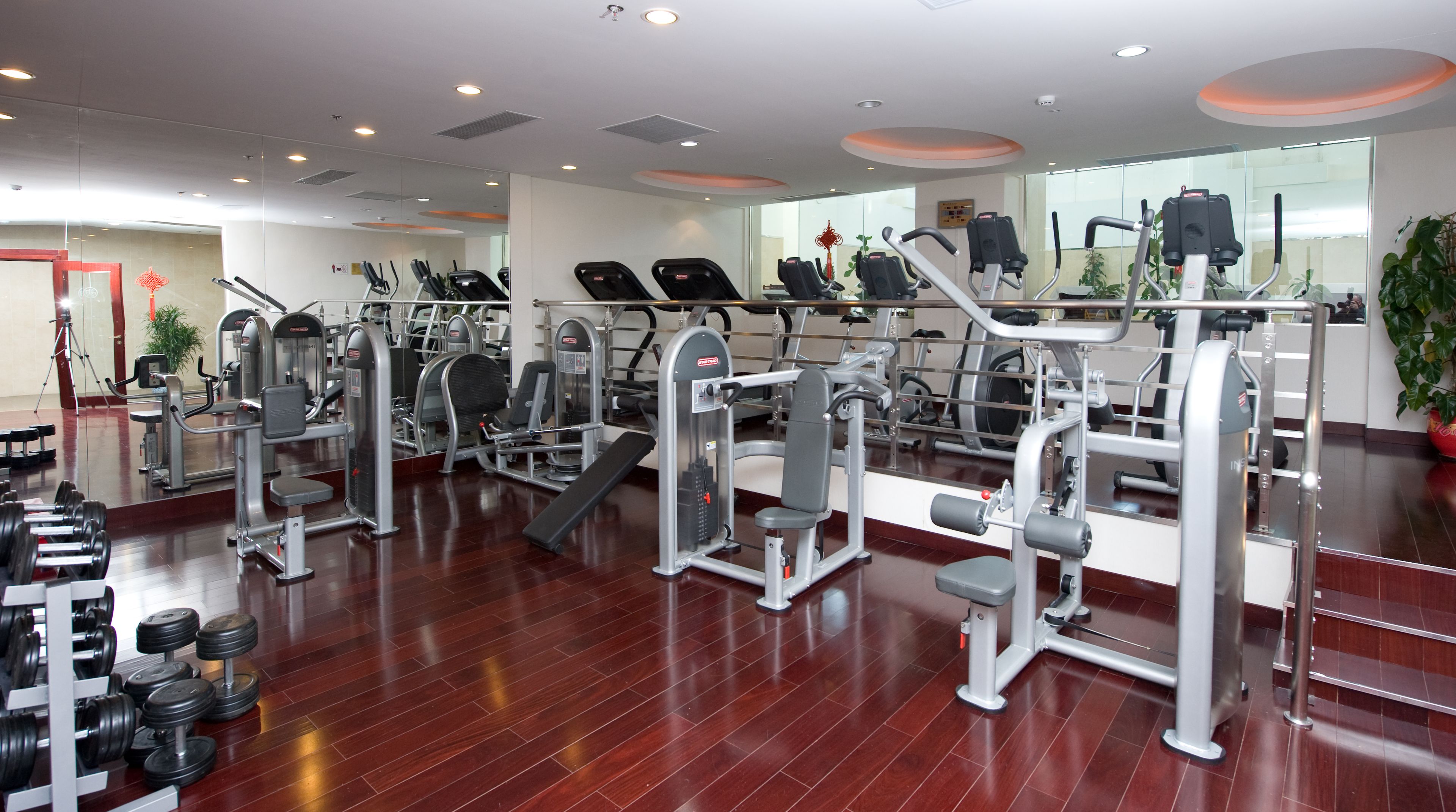 A gym with various exercise machines, a mirrored wall, and a wooden floor.