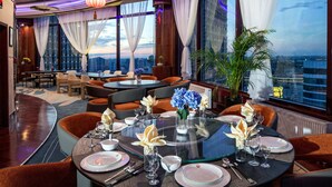 Un comedor moderno con una mesa redonda dispuesta para cuatro personas, rodeada de sillas acolchadas. La habitación cuenta con un techo curvo con iluminación integrada y ventanas amplias con cortinas traslúcidas.